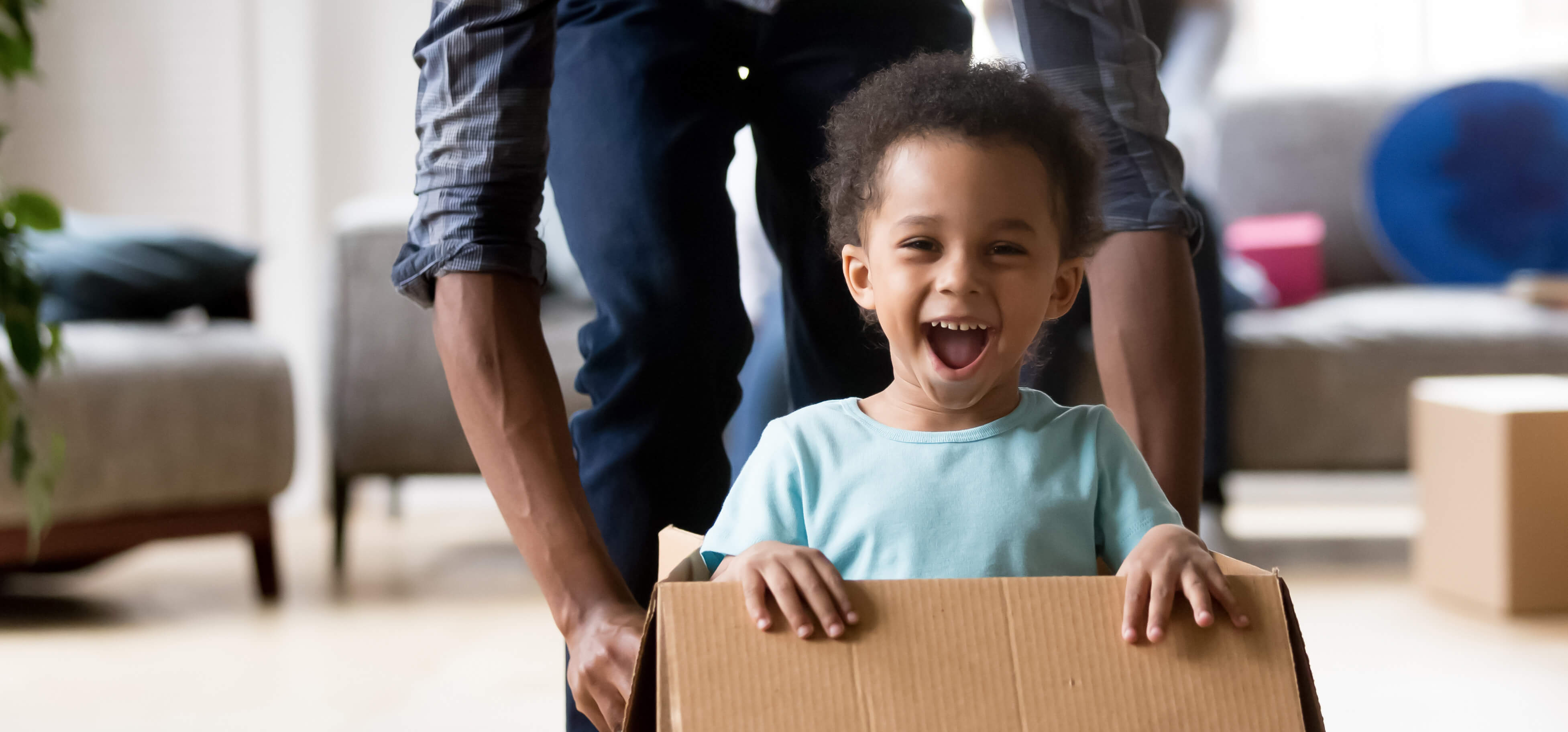 Smiling child in a cardboard box indoors with Babelio baby products in a living room setting