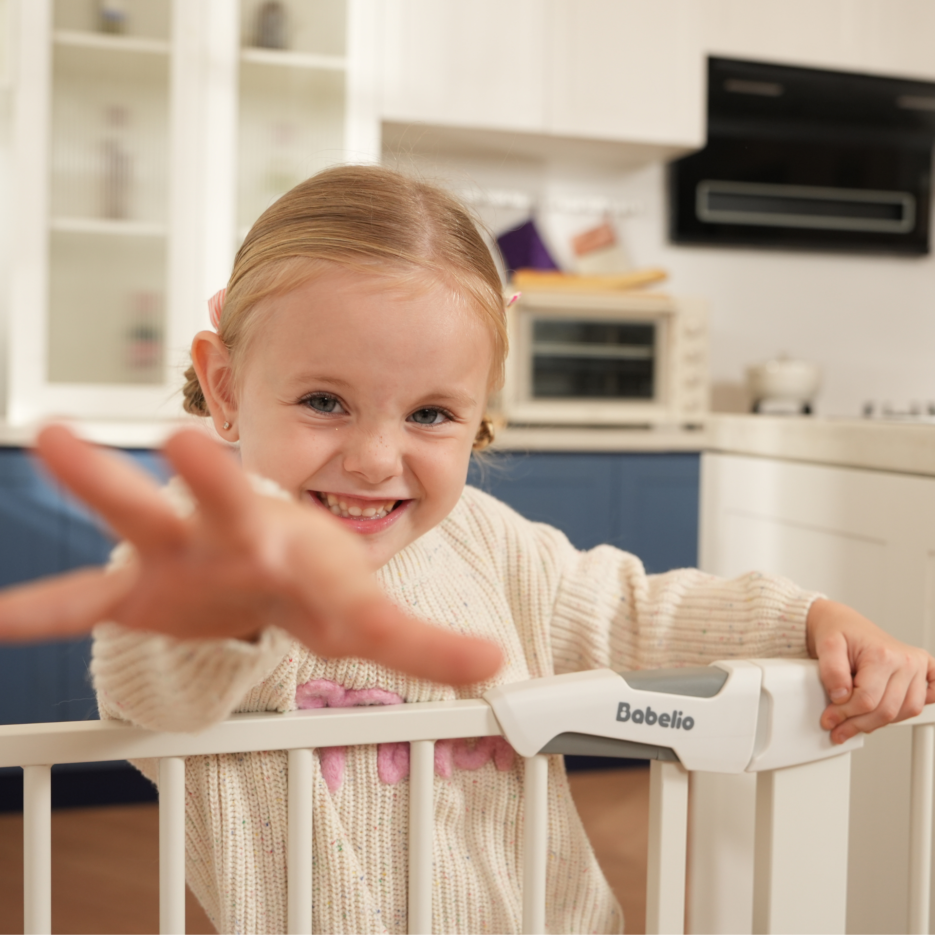 Child reaching out towards a hand held by an adult, with a Babelio baby gate in the foreground.