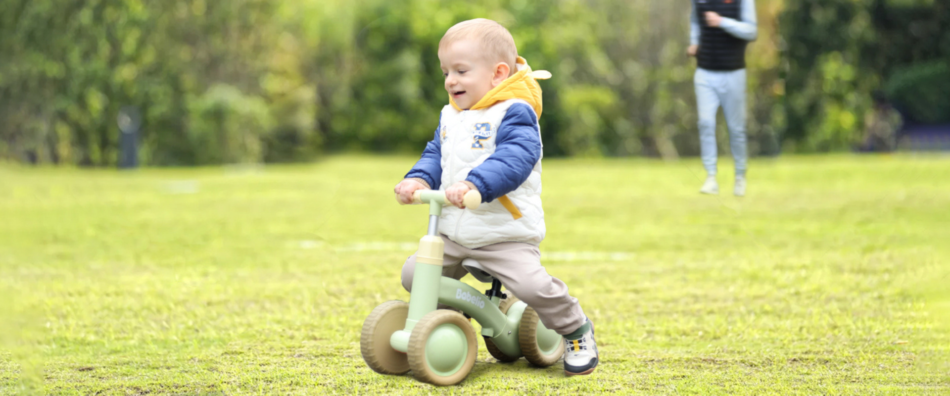 A toddler gleefully riding a Babelio balance bike on the grass, perfect for first birthdays and holiday gifts.