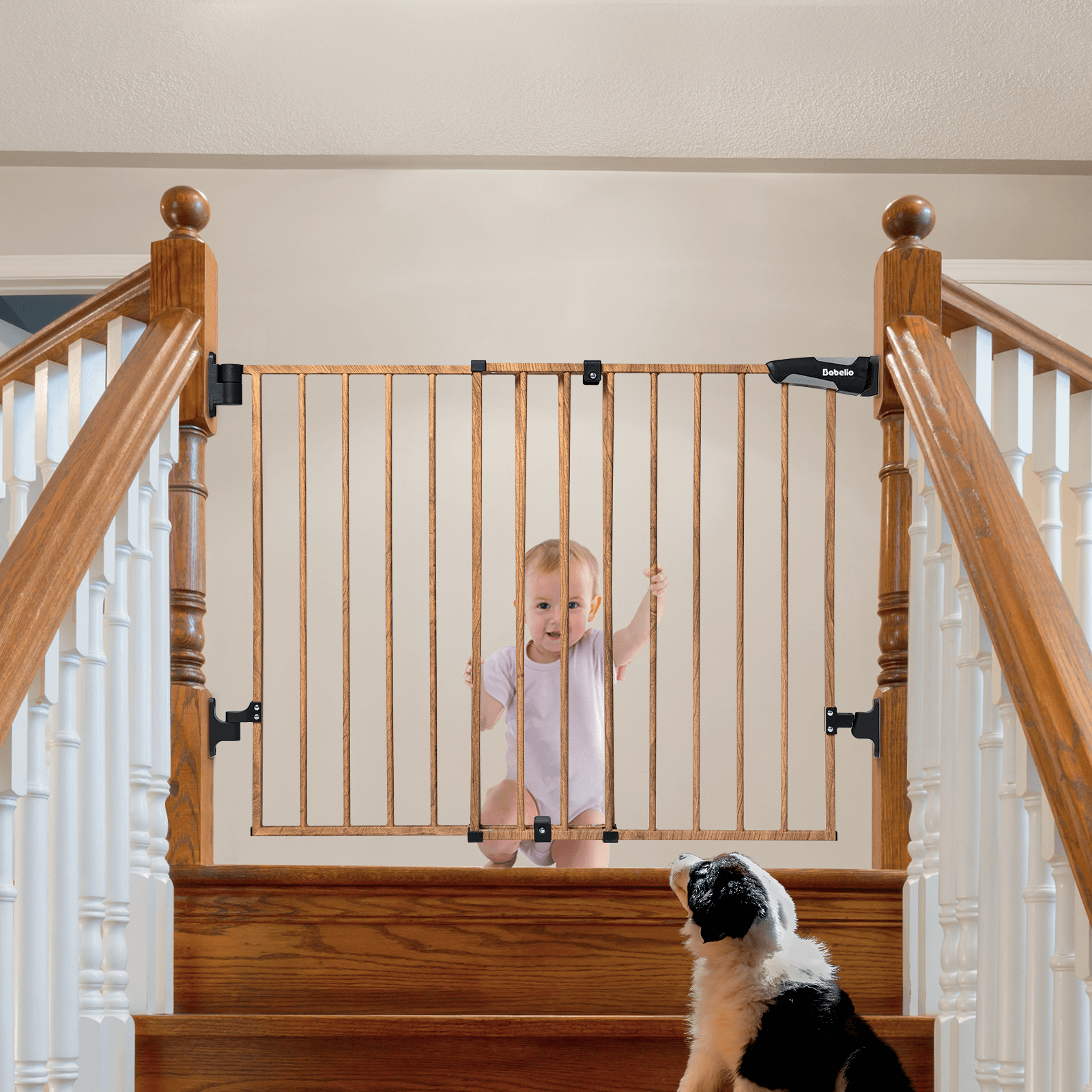 A metal safety baby gate with a wood pattern finish is installed on a staircase with a small child standing behind it reaching for the top step and a dog sitting at the bottom of the stairs.