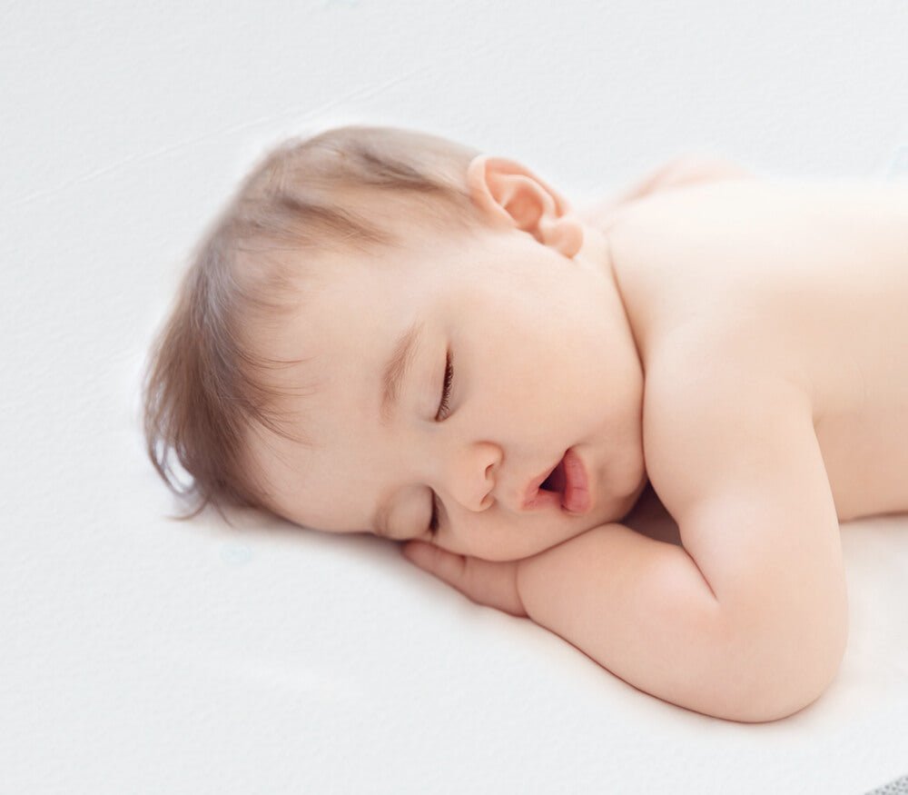 Baby sleeping peacefully on a Babelio crib mattress in a bright nursery setting