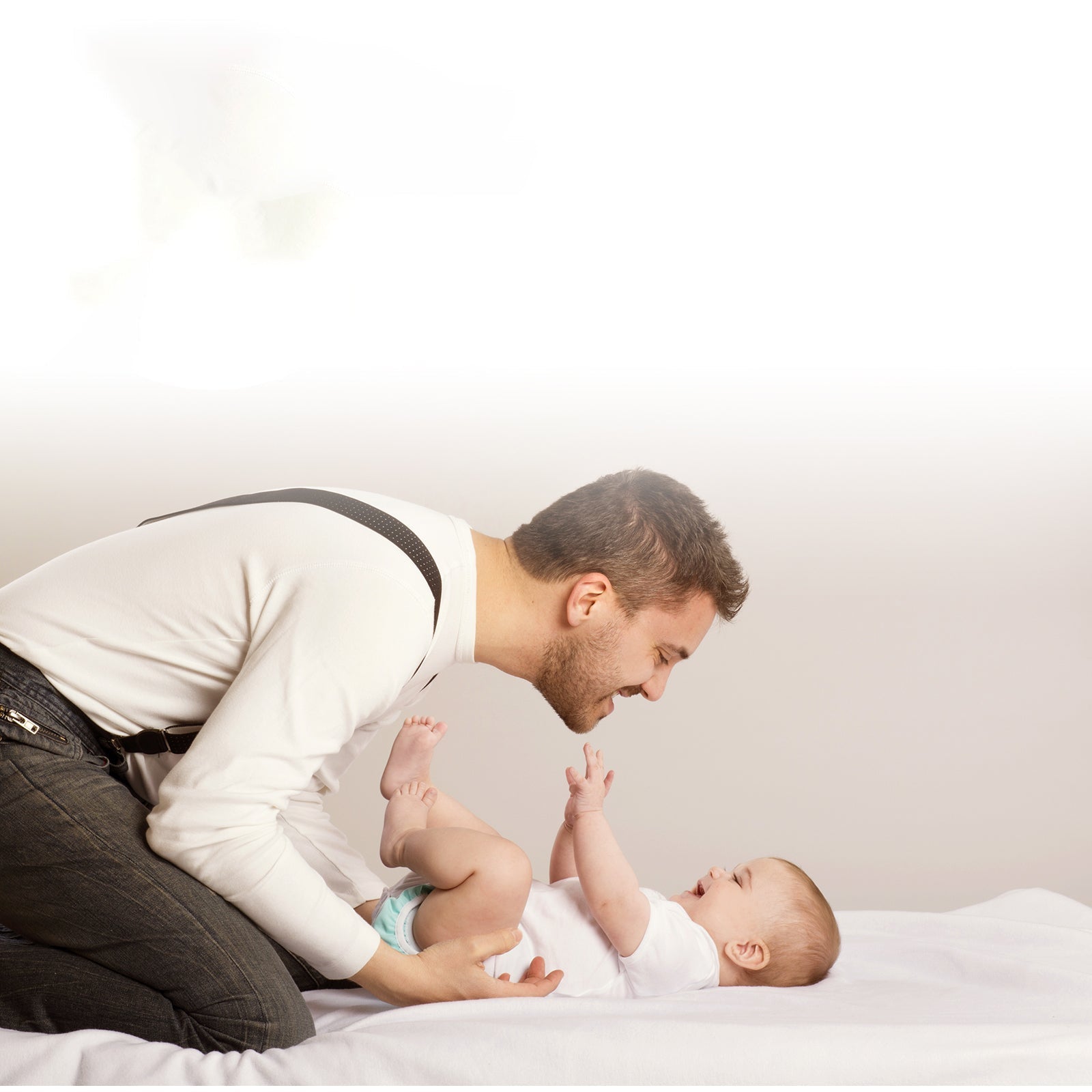 Father playing with smiling baby on a bed, showcasing Babelio baby safety and comfort products.