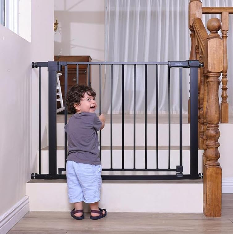 Child standing next to a black metal gate at the top of a staircase.#Color_Black