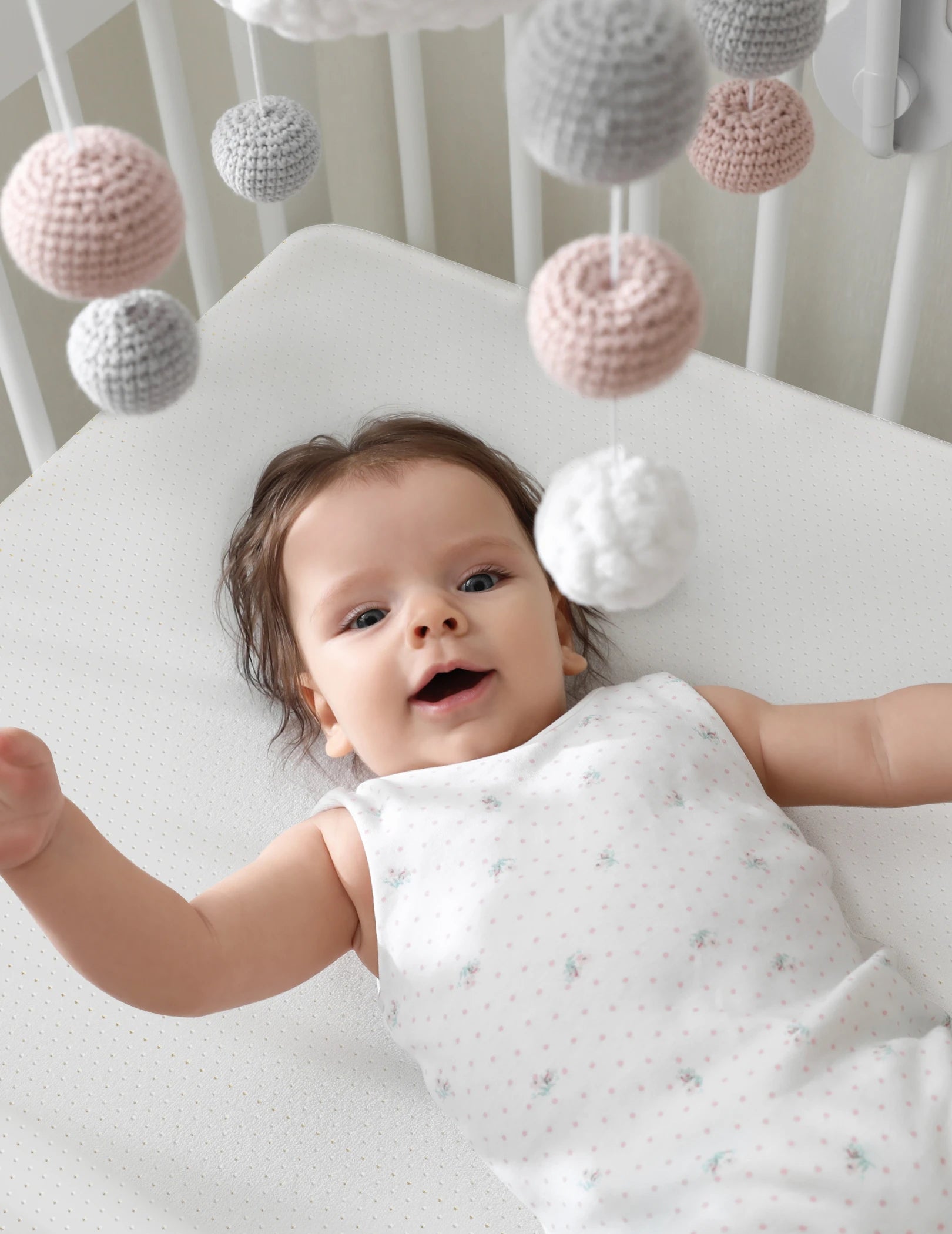 Baby lying on Babelio crib mattress in a nursery with mobile overhead