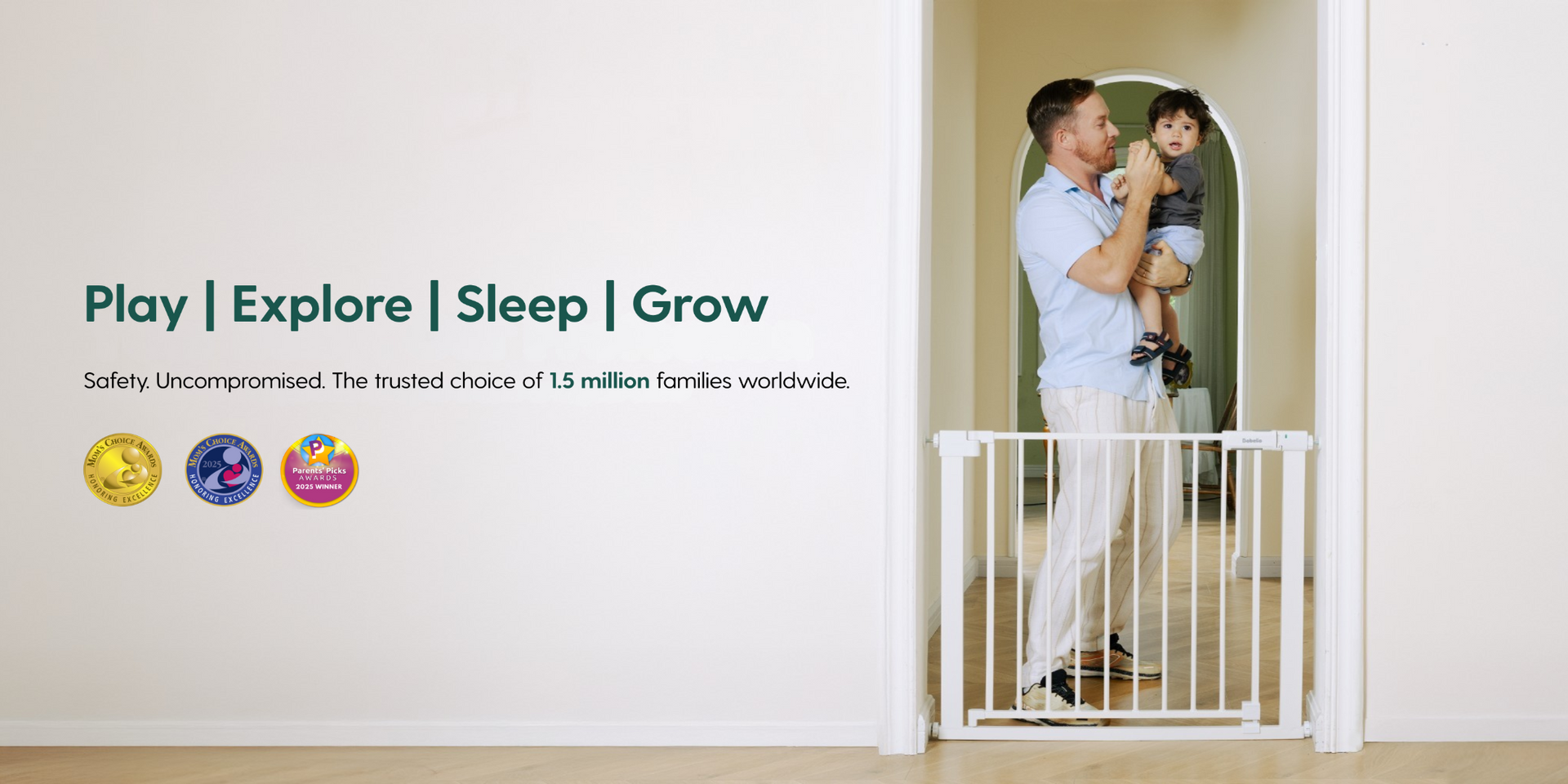 Man holding a child next to a baby gate with safety certification logos on a wall.