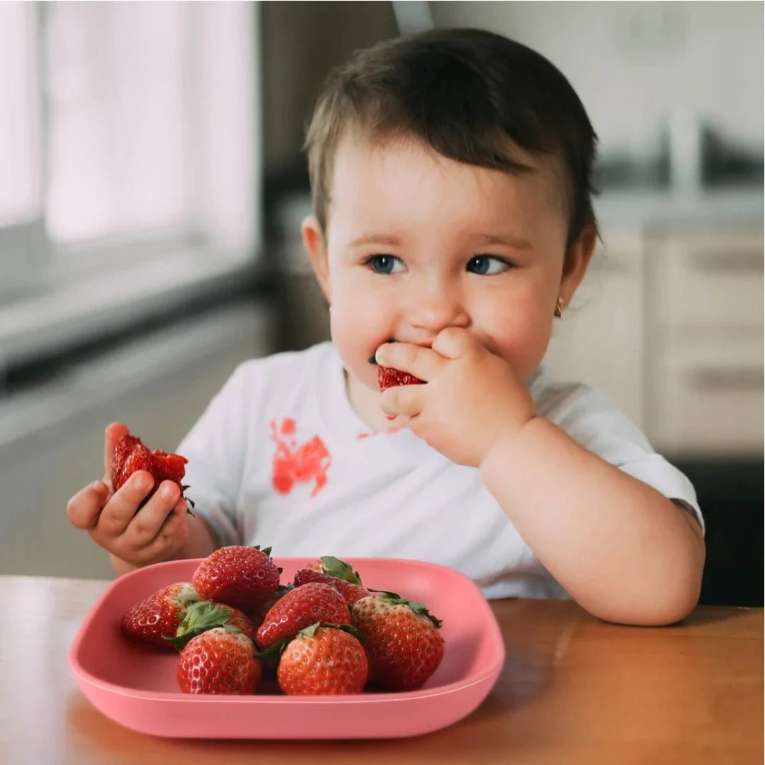 Babelio pink silicone toddler plate with strawberries, child eating in a kitchen setting