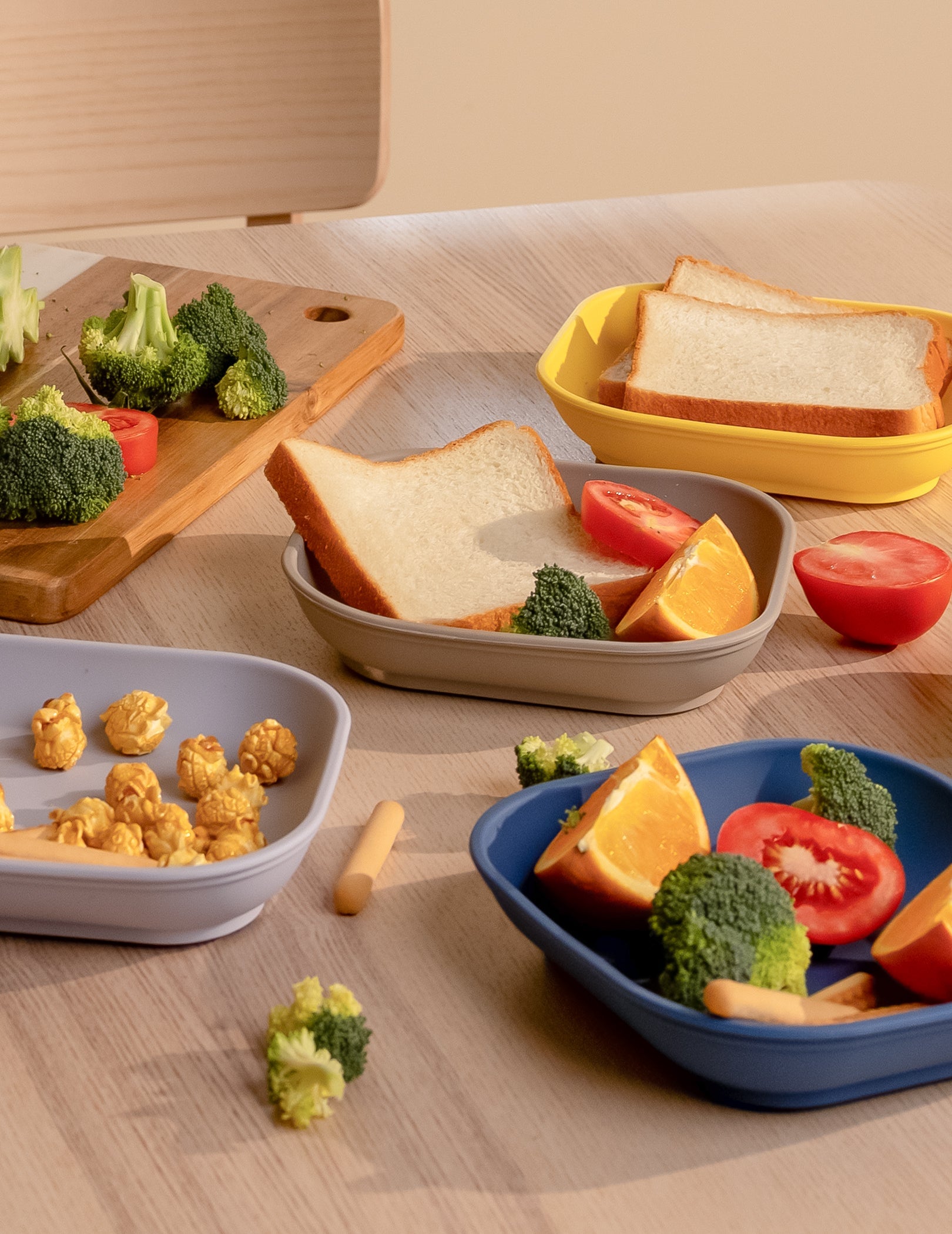 Babelio kids plates with bread, broccoli, tomato, orange, popcorn in a modern kitchen