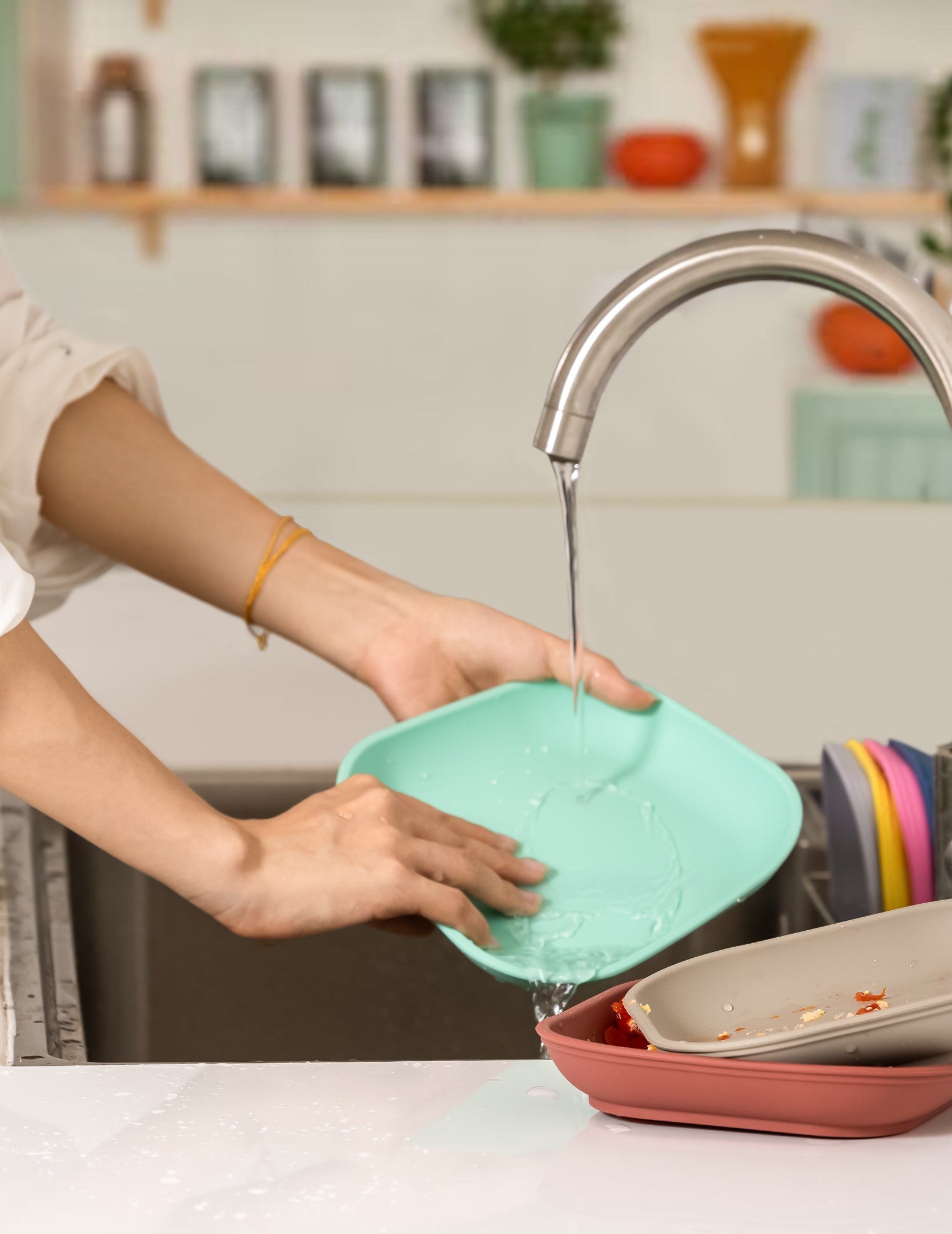 Person washing colorful baby plates, Babelio kitchen setting, running faucet