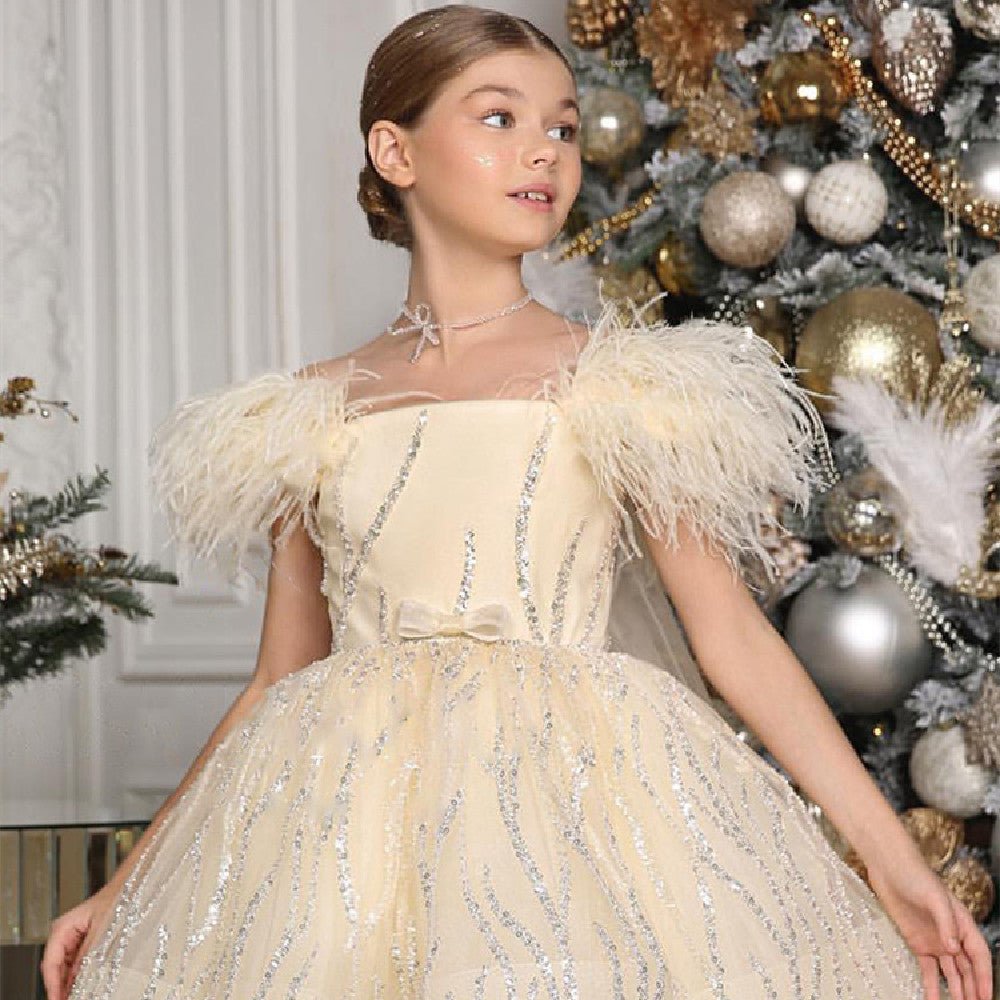 Girl in cream feathered dress posing by decorated Christmas tree with gold ornaments