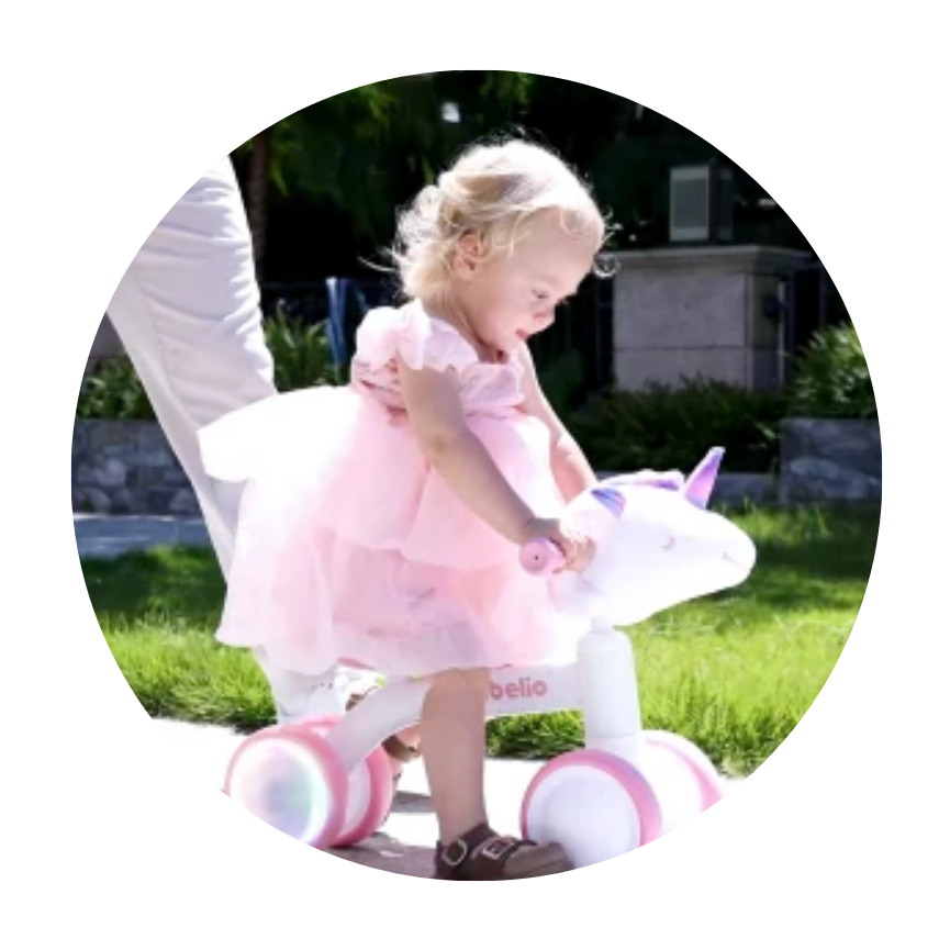 Child in a pink dress riding a toy unicorn balance bike on a grassy area