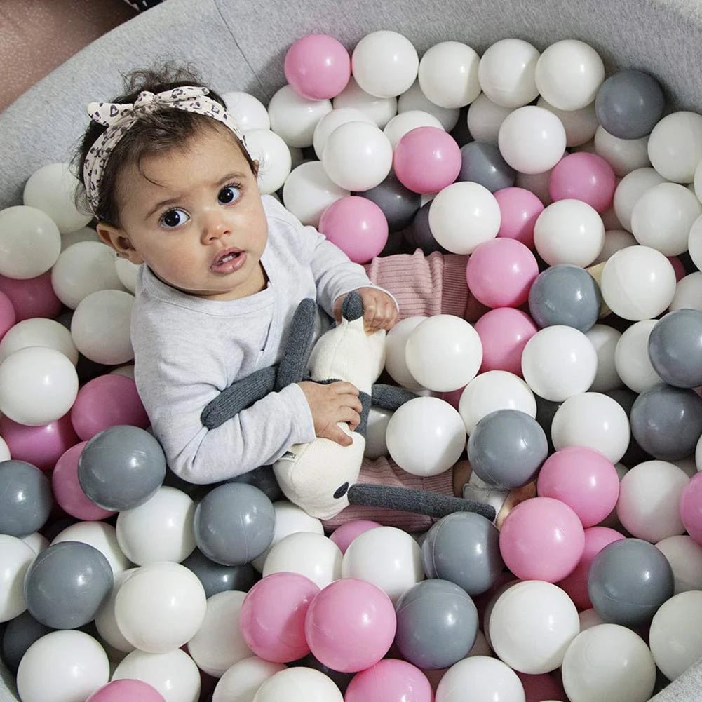 Babelio baby playing in indoor ball pit with pink, white, and gray balls, nursery setting