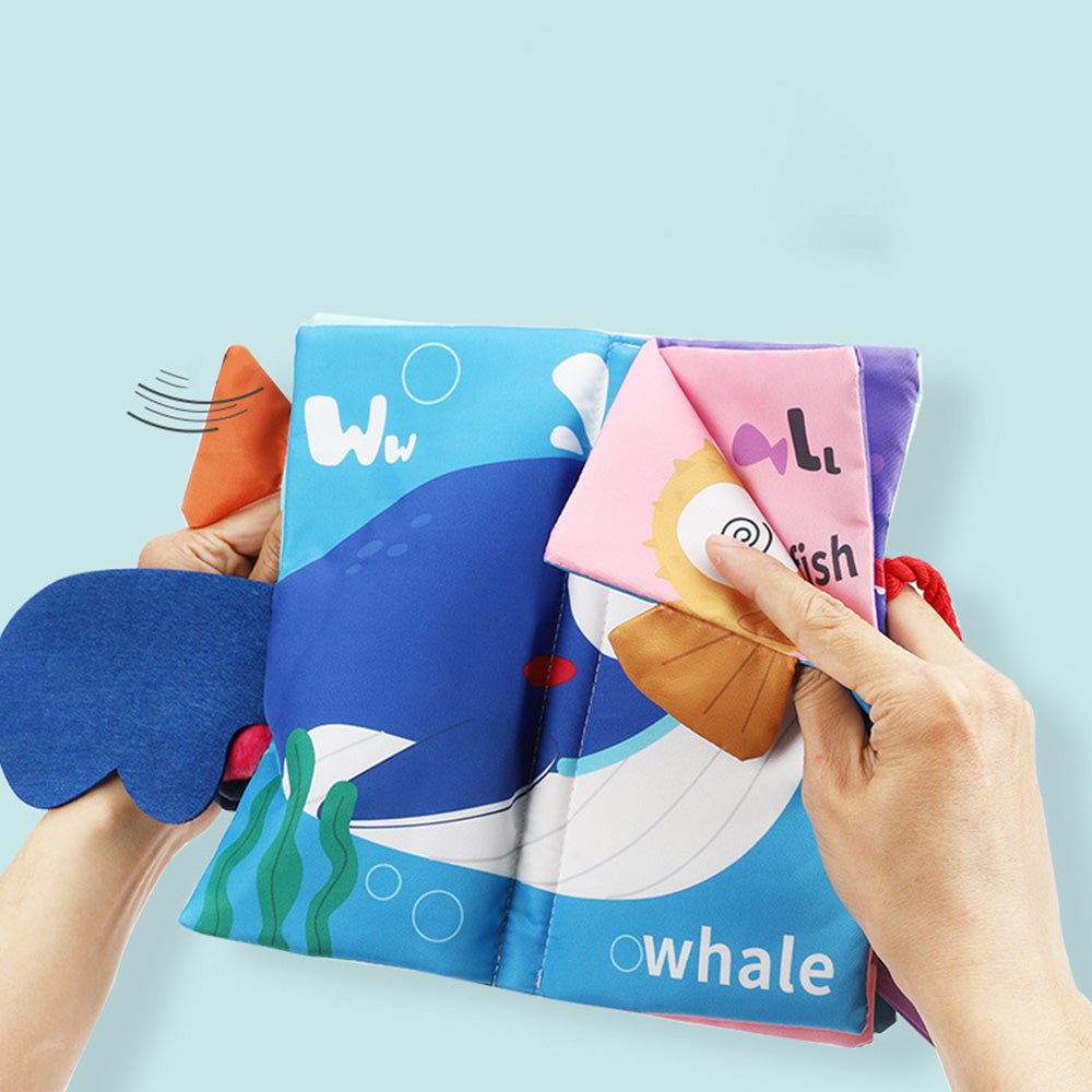 Babelio soft baby cloth book with whale and fish illustrations, hands flipping pages
