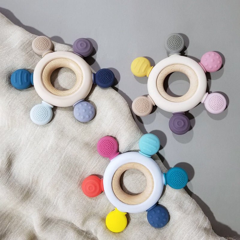 Babelio wooden and silicone baby teethers in pastel colors on a soft fabric background