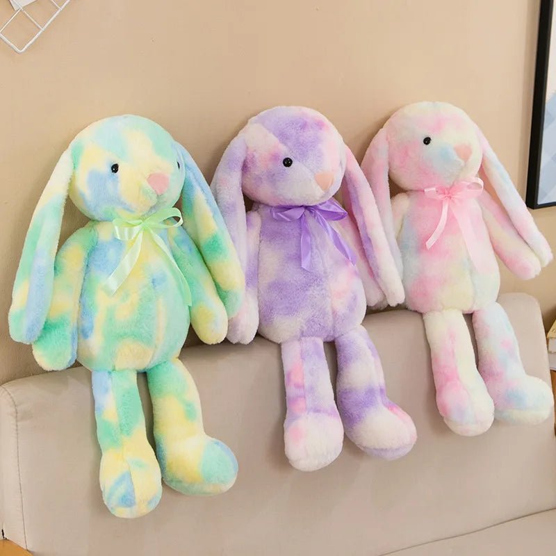 Babelio pastel plush bunny toys with bows on a beige sofa in a modern nursery setting
