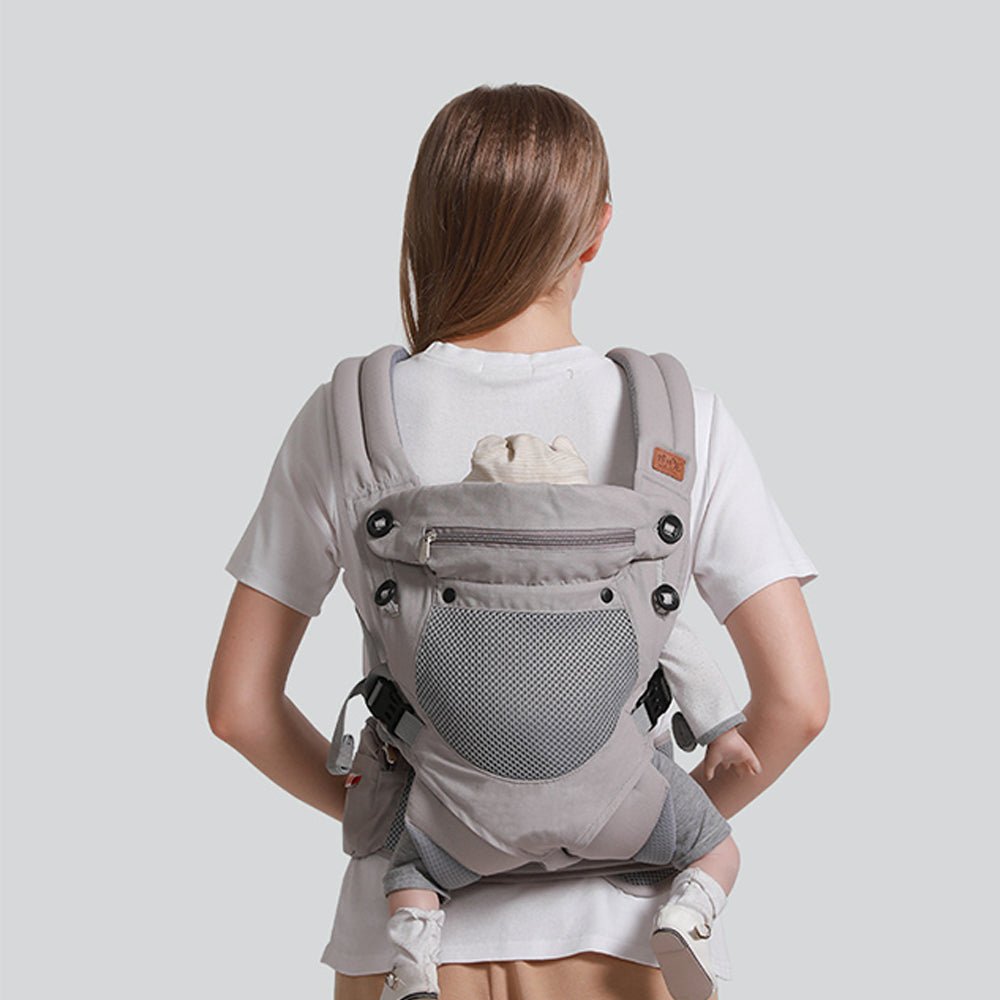 Babelio ergonomic baby carrier with hip seat in grey, worn by a woman in a plain setting