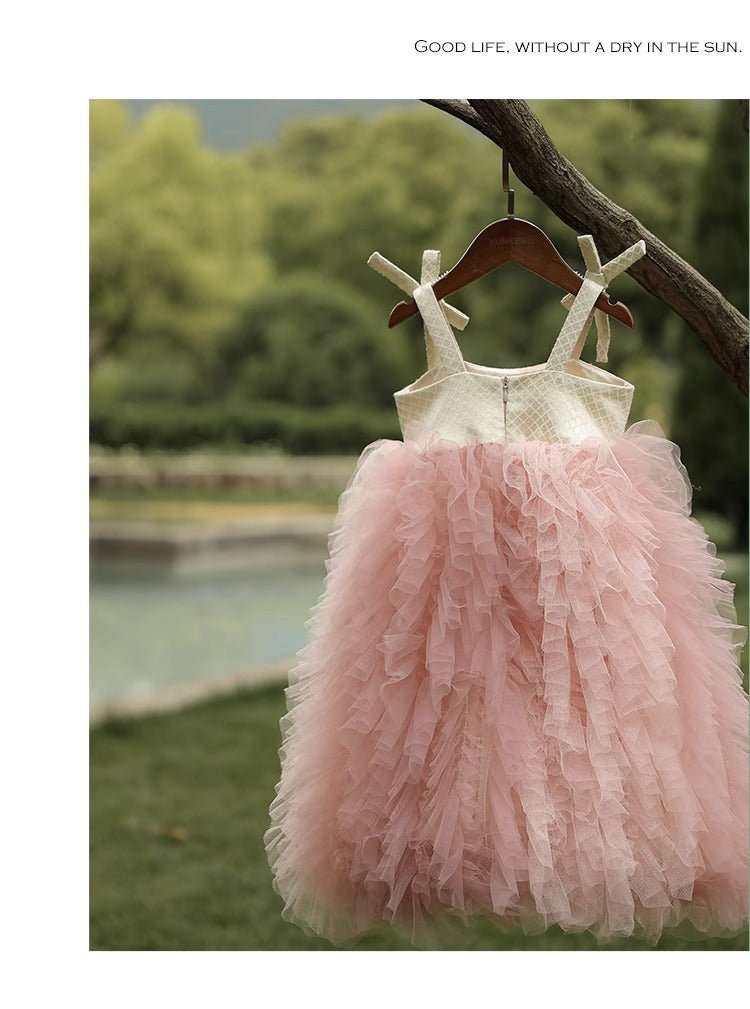 Pink tulle baby dress hanging on a tree branch outdoors near a garden pond