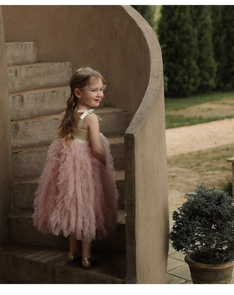 Babelio baby wearing a pink ruffled dress on outdoor stone staircase, garden background
