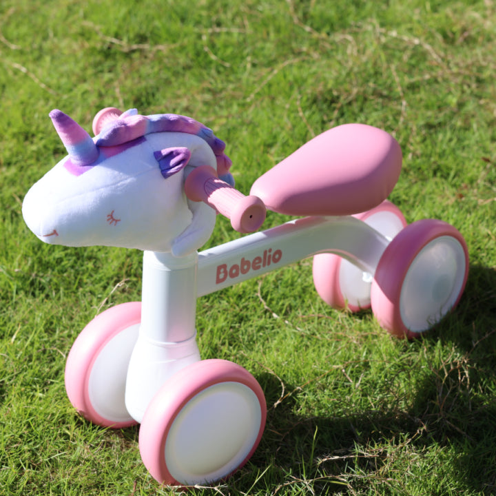 Pink and white toddler balance bike for 1–3 year old girls, featuring a plush unicorn head and LED glowing wheels, shown on grass to highlight outdoor play fun from the Magic Ride series by Babelio.